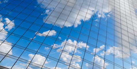 Reflection of a blue sky with white clouds on the glass wall of a skyscraper in the business center of the cityscattered throughout