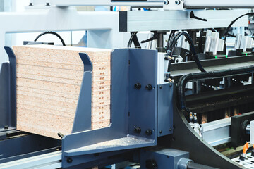 A stack of white boards are being cut by a machine. The boards are all the same size and are lined up on a conveyor belt