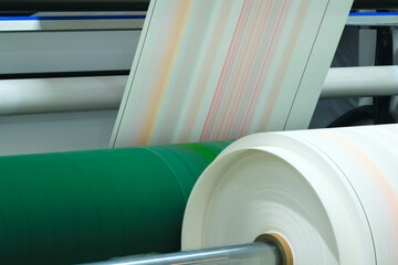 A roll of paper being printed on a machine. The rolls of paper are stacked on top of each other,...