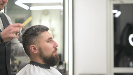 Haircut of a visitor in a barbershop. Hair styling with a hand, combing the client's hair by a stylist.