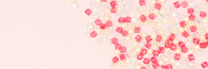Different acrylic beads scattered on a pink background. Banner with copy space.