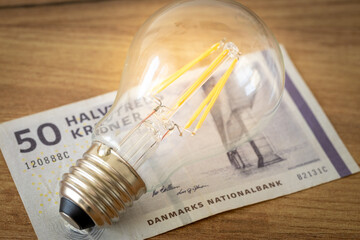 Glowing light bulb lying on Danish money, Concept, Electricity price increases, Denmark home...