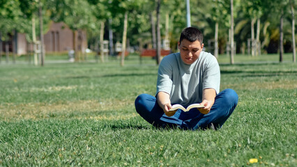 Obraz premium Young man reading a book sitting on the grass