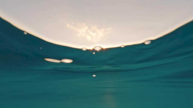 Swimming at sea during sunset, paragliding in the sky, half camera underwater, dark water visible
