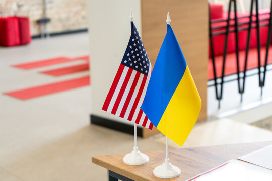 Flag of Ukraine and USA in office background. Table stand flagpole. - Powered by Adobe