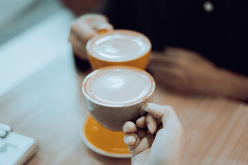 Close-up of a man and woman clinking coffee cups while talking at work.