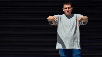 Young man making disapproval hand sign on black background, dislike, negative 