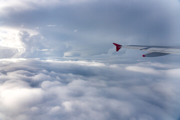 Wings of an airplane flying between clouds at sunset.