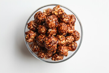 Chocolate popcorn, in transparent glass bowl, isolated on white background, flat lay or top view