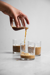 Vertical of a hand pouring coffee into a glass with ice, with additional glasses in the background