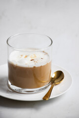 Close-up vertical shot of a glass of cappuccino with frothy milk and a golden spoon on a white plate