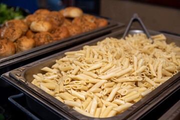 Chef serving tasty mix of pasta. Event catering close up in a metal armer. 