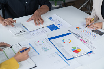 A photograph of a male and female employee's hands as they meet in an office, pens and laptops at the ready as they consult on business matters.