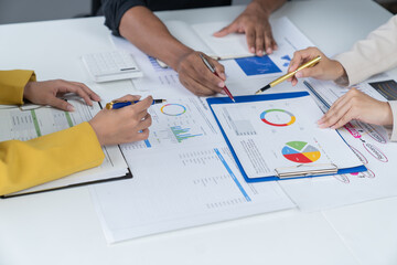 A photograph of a male and female employee's hands as they meet in an office, pens and laptops at...