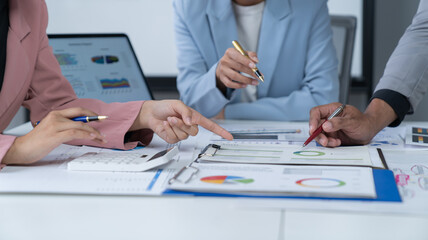 A photograph of a male and female employee's hands as they meet in an office, pens and laptops at the ready as they consult on business matters.