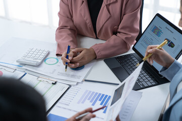 A photograph of a male and female employee's hands as they meet in an office, pens and laptops at the ready as they consult on business matters.