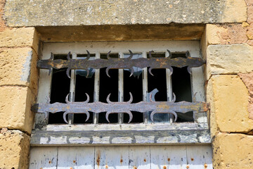 Ancient shabby weatherworn window with broken glass and rusty wrought iron security bars in a French medieval village

