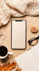 Smartphone mockup with blank screen, cup of coffee, paper notebook, blanket and feminine accessories on beige background. Home office desk table concept. Flat lay, top view.