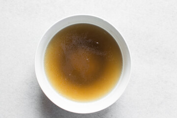 Overhead view of chicken broth in a white bowl, top view of cooked chicken beef broth, process of making broth