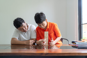 Fototapeta premium Asian father and son playing wood blocks game Carefree kid playing wood blocks game building constructor from blocks with father at home