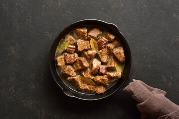 Braised beef in cast iron skillet over dark stone background