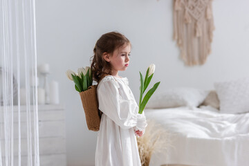 Close-up portrait of a little girl in a white dress, nightgown. Toddler embraces a bouquet of...