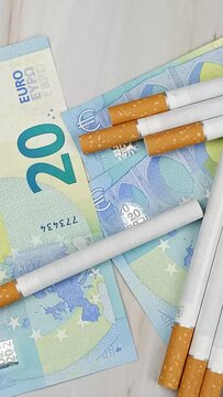 plusieurs cigarettes et billets de vingt euros, en gros plan, vue du dessus.