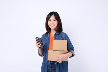 Naklejka premium young asian woman wearing orange t-shirt and denim shirt holding parcel box while using a smartphone isolated on white studio background, Delivery courier and shipping service concept.