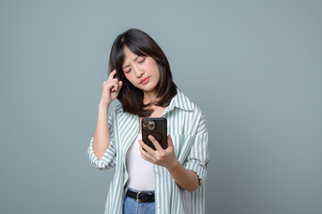 Asian woman holding smartphone and looking with doubt, disappointed with mobile phone app, standing against green background