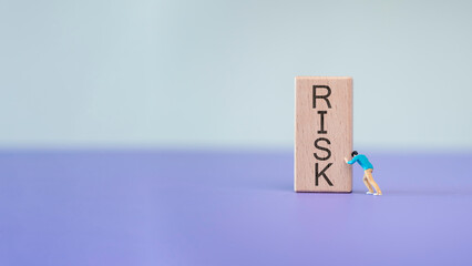 a miniature figure pushing against a wooden block with the word 'RISK' written on it. symbolizes the concept of facing and managing risk in business or personal endeavors