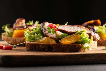 Tasty homemade sndwiches with grilled vegetables and sausages and fresh juicy salad leaves on the serving board close up.
