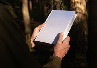 . Male hands holding book hardcover, blank hard cover mock up in nature.