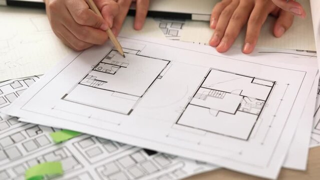 Professional engineer team discussion about house design on meeting table with architectural equipment and building blueprint scatter around at modern office. Focus on hand. Closeup. Delineation.