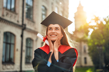 A happy graduate holding a diploma in front of a university building on a sunny day