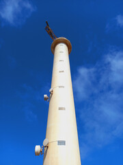 Obraz premium White lighthouse shining in the clear sky. An old white brick lighthouse seen from below. High tower on the coast that serves for safe navigation at night.
