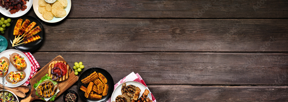 Poster Summer BBQ or picnic food corner border. Burgers, grilled meats, potatoes, corn ribs, fruit, salad and snacks. Overhead view on a dark wood banner background. Copy space.