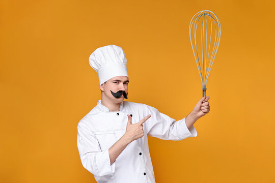 Pastry chef with fake mustache pointing at big whisk on orange background - Powered by Adobe