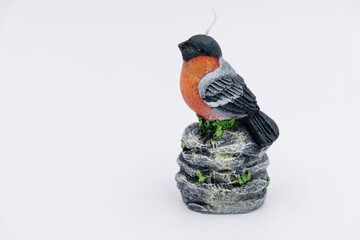 Close-up side view of handmade wax candle in shape of male bullfinch bird with red plumage sitting...