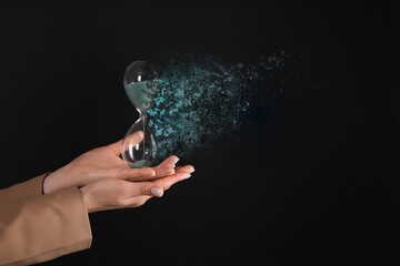 Businesswoman holding dissolving hourglass on black background, closeup. Time is running out