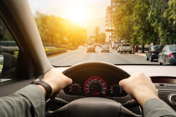 Driving car, view from driver's seat. Man holding hands on steering wheel, closeup
