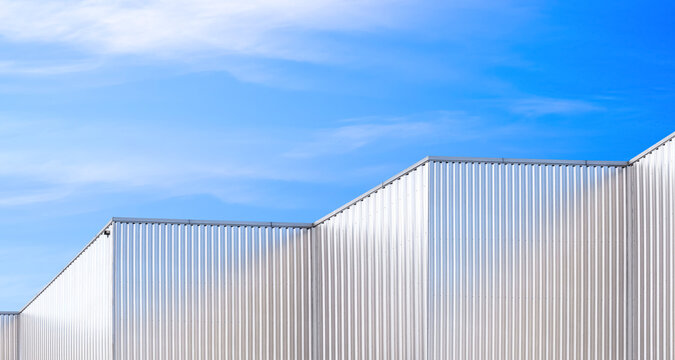 Row of aluminium corrugated metal wall of geometric industrial factory buildings against blue sky background, low angle and perspective side view