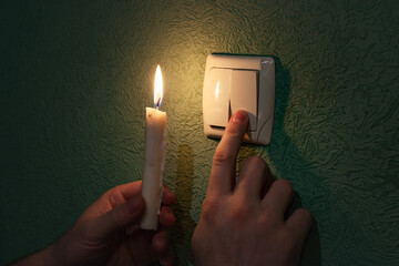 Holding burning candle in a dark room near a light switch, blackout. 
Power outage, energy crisis....