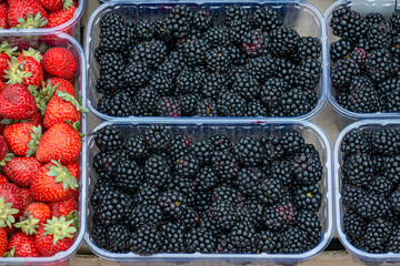 Ripe blackberries and strawberries in plastic containers. Food market. Counter with plastic containers filled with fresh berries.