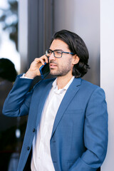 vertical image of A young businessman wearing glasses and blue suit talking on a cell phone outside