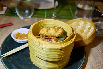 Fried wontons in oriental bamboo steamer on wooden table of restaurant ready to eat