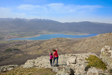 Mother and daughter at the top of the mountain pointing to the Pinilla reservoir, the Lozoya valley and the mountains of the Guadarrama National Park, in Madrid, Spain