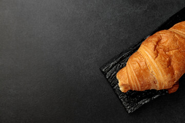 Crispy hot croissant on a black rectangular wooden board on a gray background