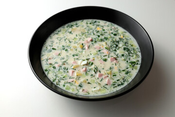 Cold soup with fresh cucumbers, sausage, broth and sour cream in a black plate on a white background. A traditional dish is okroshka.