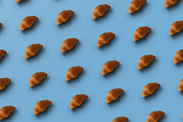 Naklejka premium Pattern of baked croissants with a blue background. Delicious pastries