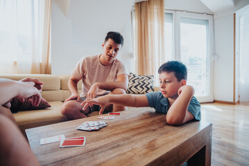Obraz premium Family members gather around a wooden table in a cozy living room, enjoying a relaxing session of playing card games.